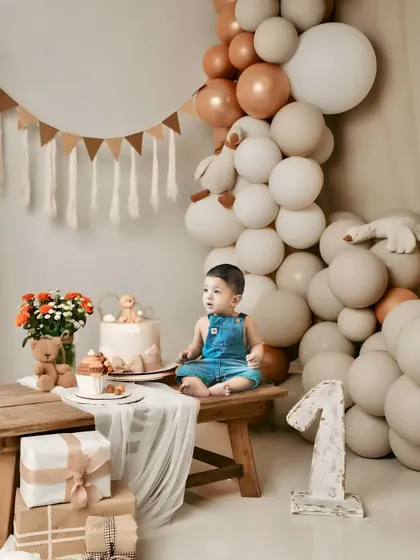 A classic first birthday studio portrait. The neutral tones of the balloons and props keep the focus on the birthday boy and the big number one.