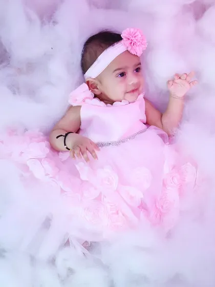 An ethereal, dreamy shot of the baby girl lying back in the pink-lit clouds.