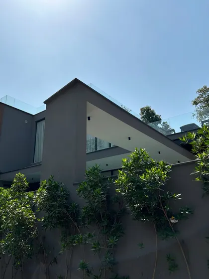 The upper volume of Gulmohar Farmhouse features a deep, cantilevered balcony that creates a dramatic architectural statement. The dark grey finish and glass railing give it a modern, almost sculptural quality against the sky.