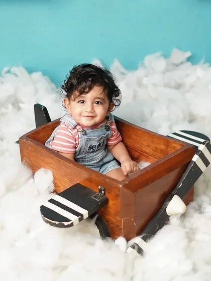A full shot of the little pilot in his wooden plane, surrounded by fluffy clouds. This theme is perfect for capturing a child's sense of adventure.