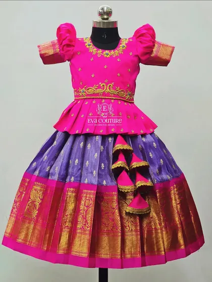 A classic pattu pavadai in pink and lilac. The pink peplum top has delicate gold embroidery, and the lilac skirt has a traditional gold and pink border.