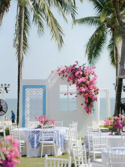 A dreamy beachside wedding setup in Thailand, featuring a white and blue Santorini-inspired theme with lush pink bougainvillea for a pop of color.