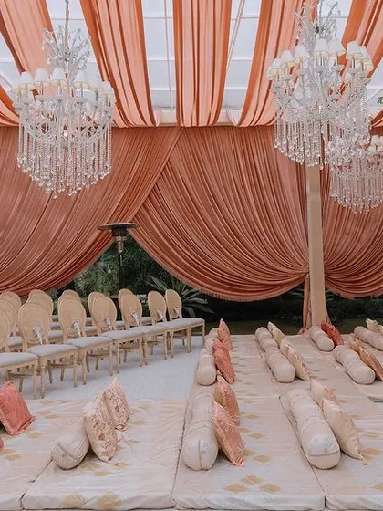 The ceremony seating was a mix of classic chairs and floor seating with custom-printed cushions. The space is defined by peach-colored drapes and magnificent crystal chandeliers.