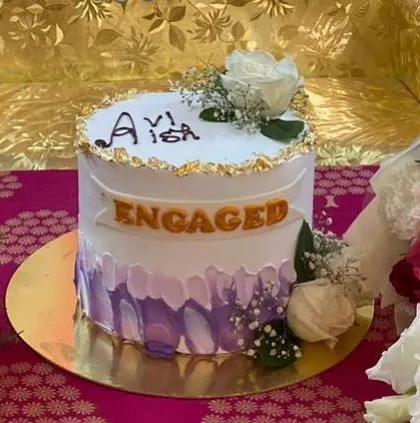 This lovely engagement cake features a soft purple brushstroke effect and is topped with fresh white roses. The "Engaged" banner makes it a clear and beautiful announcement of your special news.