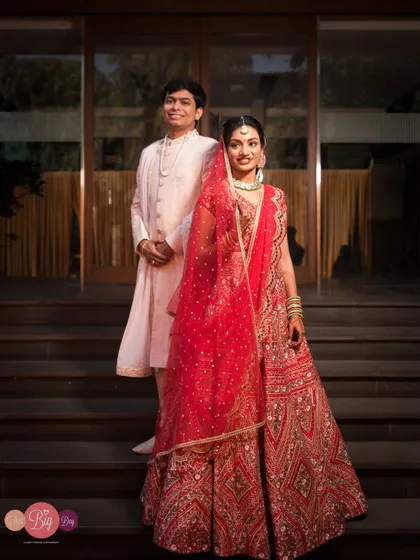 A regal portrait of Arpita and Mahesh on their wedding day, showcasing their stunning red and white outfits.