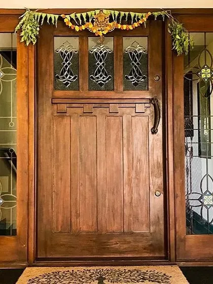 This solid wood entrance door, framed by glass panels with traditional motifs, offers a grand welcome to the Roopa Hariprasad Residence. The design balances strength and elegance, reflecting the home's blend of modern and classic styles.