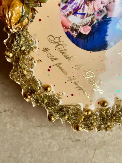 A close-up of an elegant flower photo frame. This custom piece showcases wedding flowers around a beautiful photo, with names and a date in golden perfection.