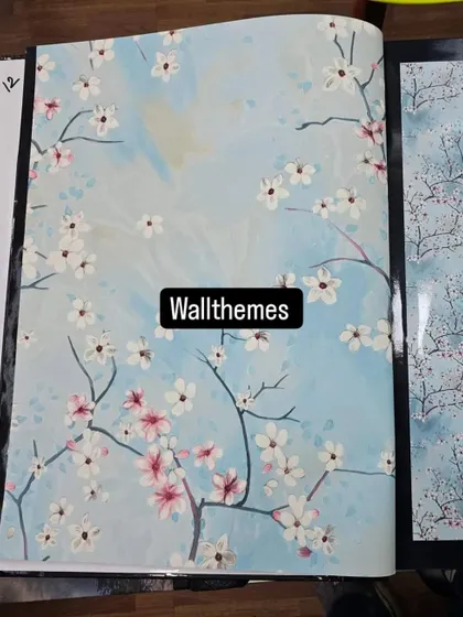 A sample of a cherry blossom wallpaper with a light blue background, shown in a catalog book.