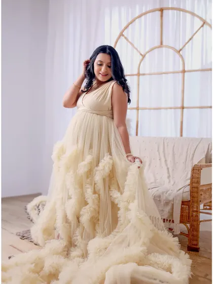 A full-length portrait of a mom-to-be in a cream-colored ruffled gown in our bright and airy boho studio.