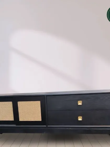A modern console table featuring a black finish with woven cane sliding doors and brass pulls. This design blends contemporary and natural elements, offering a stylish and versatile storage piece.