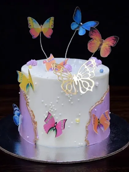 A whimsical butterfly-themed cake. This design features a purple fault line with a gold edge, and is decorated with colorful edible wafer paper butterflies and a gold acrylic butterfly.