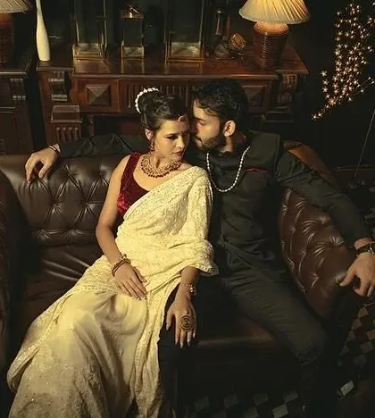 A romantic and cozy portrait of a couple embracing on a couch, with warm lamp lighting creating a classic, cinematic feel.