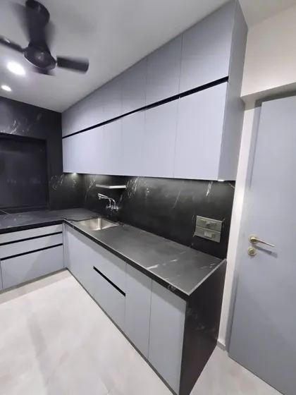 An L-shaped kitchen layout featuring handleless light grey cabinets and a contrasting black marble countertop and backsplash. The design emphasizes clean, horizontal lines for a minimalist and modern aesthetic.