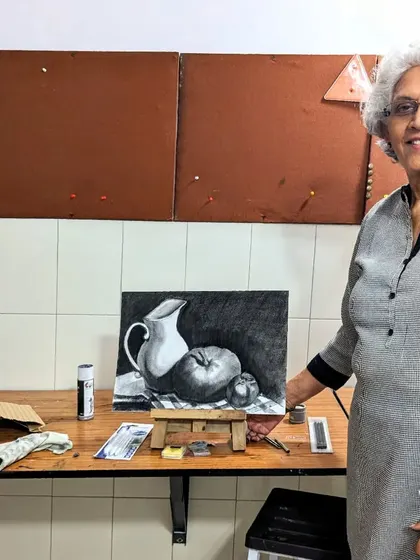 It's never too late to pursue a passion for art. One of our adult students from a hobby class proudly stands with her completed charcoal still life, a testament to her dedication and progress.