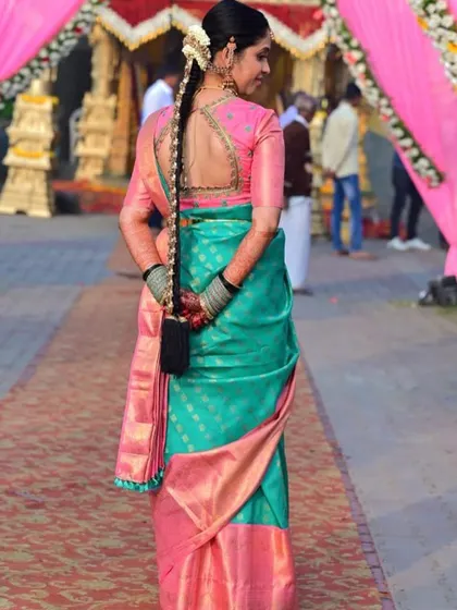 A side profile of the bride's custom blouse, showing the sheer back with intricate embroidery. This design adds a modern touch to the traditional pink blouse, pairing beautifully with her teal and pink saree.