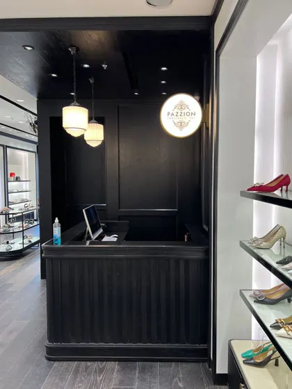 The billing counter, designed with dark wood paneling and a custom circular lightbox featuring the Pazzion logo. This creates a strong, branded checkout experience.