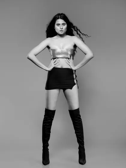 A powerful full-body black and white shot of a model in a gold top, mini skirt, and thigh-high boots. This is a classic high-fashion pose with a strong silhouette.