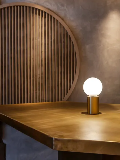 Simplicity in design. A single, elegant lamp on a brass-topped table, set against a backdrop of clean lines and natural textures.