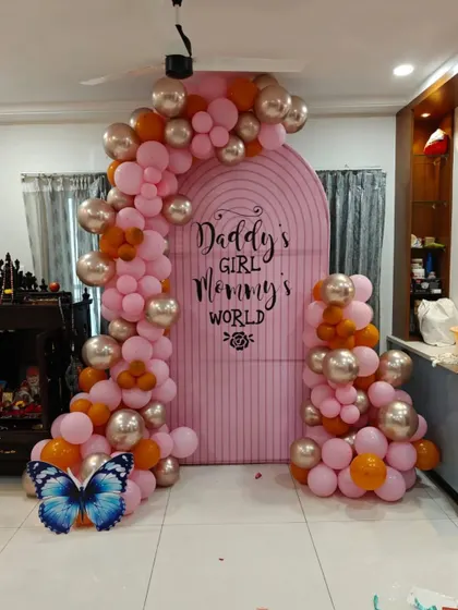 A sweet "Daddy's Girl Mommy's World" backdrop for a baby girl's celebration. The pink arched backdrop is decorated with a pink, orange, and gold balloon garland.