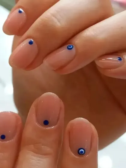 A minimalist and chic design with a sheer nude base and tiny, simple evil eye and dot details.