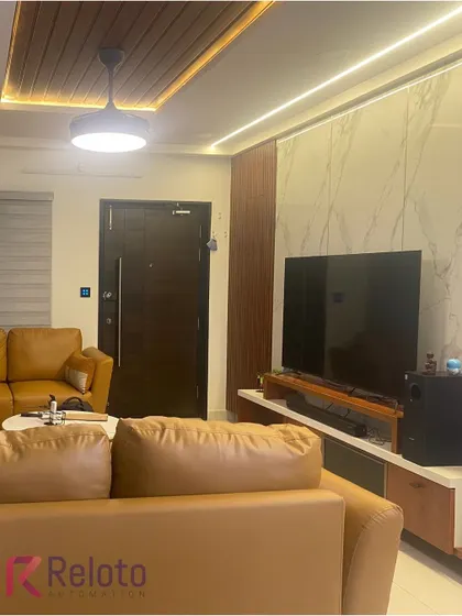 This living room combines comfort with smart technology. The television area is complemented by automated ceiling and accent lighting, all controlled via discreet wall panels and a central app for a seamless entertainment experience.