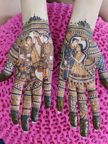 A beautiful and detailed design for an engagement, focusing on the couple's portrait on the palms. The fingers are tipped with fresh henna paste, ready for a deep, rich stain.