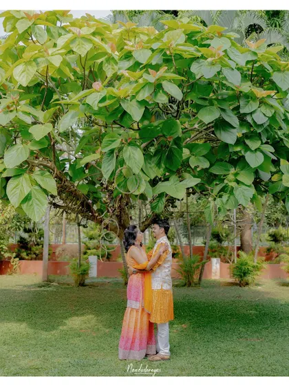 The couple stands together under a beautiful tree, a classic portrait that captures their love in a serene, natural setting.