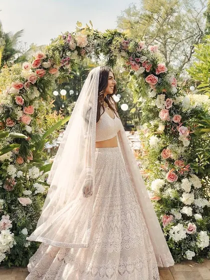 A bride posing under a beautiful floral arch, a classic and timeless element for any wedding.