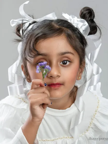 "Wrapped in innocence and ribboned with grace." A creative close-up of a girl with white ribbons in her hair, holding a flower to her eye.