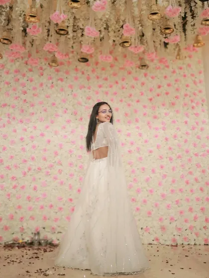 This stunning white lehenga with cape-like sleeves creates a dramatic and glamorous silhouette against a floral backdrop. It's an ideal rental for making a grand entrance.