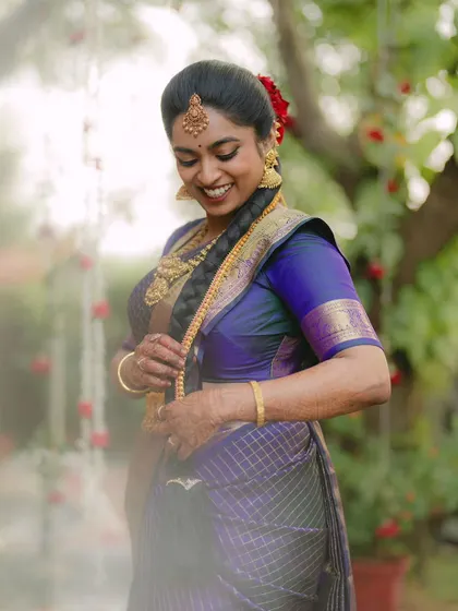 A South Indian bride, adorned in a beautiful blue and gold saree, shares a joyful, natural smile. The soft, dreamy light enhances her radiant happiness.
