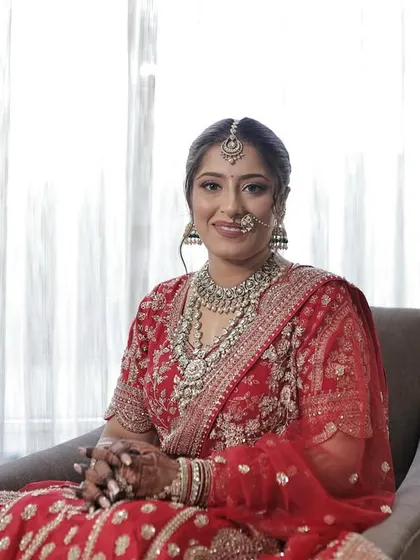 A portrait of the bride seated, with soft backlighting that highlights the flawless makeup and intricate details of her outfit.