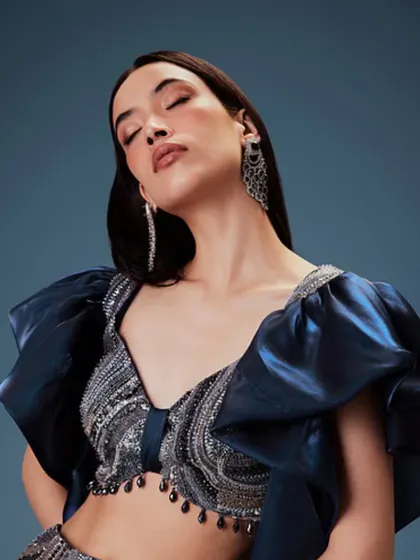 A close-up of a soft glam makeup look. The focus is on luminous skin and a neutral lip, which works perfectly with the dramatic puffed sleeves and intricate beadwork of the blouse.