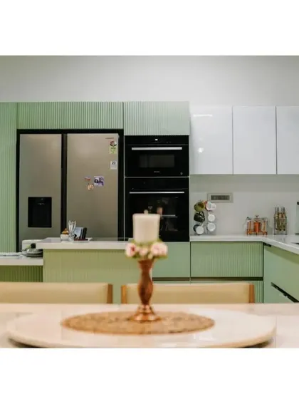 This modular kitchen design focuses on clean lines and high functionality. The combination of pastel green fluted panels and glossy white cabinets creates a fresh, modern look, with integrated appliances and an island that doubles as a breakfast counter for a practical, everyday living solution.