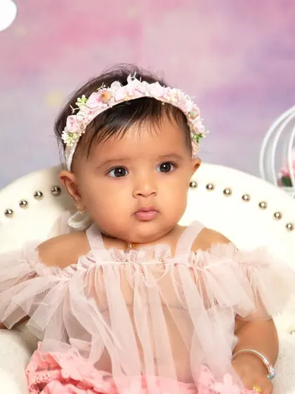 A regal portrait from a unicorn-themed half-birthday shoot. The baby sits confidently in a mini throne chair, surrounded by whimsical props like a birdcage and teepee.