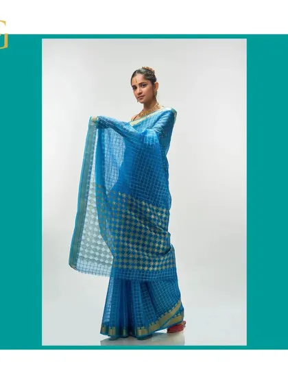 The lightness of the Persian blue organza is shown as the model holds the pallu, revealing the intricate geometric and floral design.