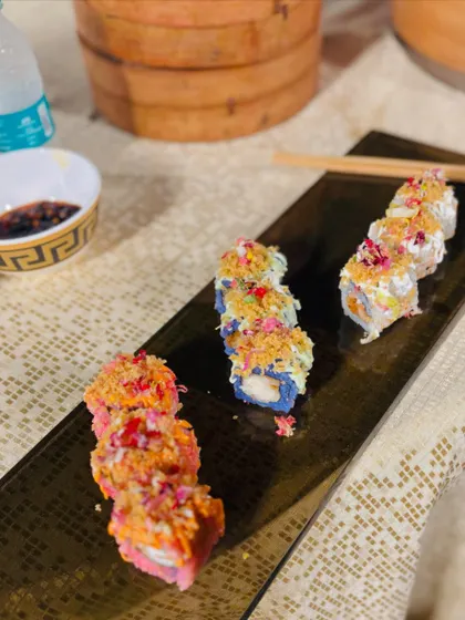 A close-up of beautifully plated sushi rolls, garnished with edible flowers and crispy toppings, ready to be served.