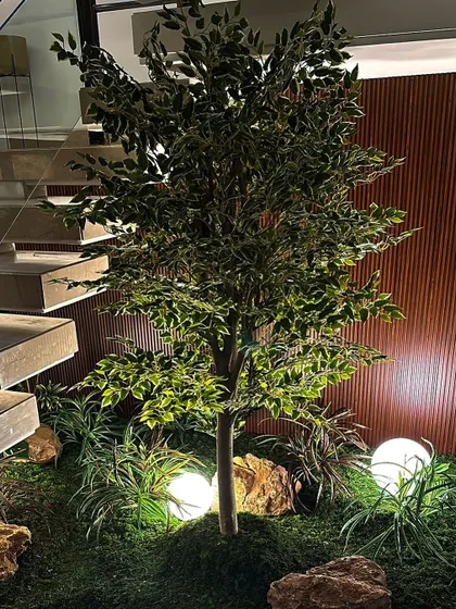 A full, leafy artificial tree stands as the centerpiece of this mossy under-stair garden. The spherical lights scattered throughout the moss bed create a whimsical, enchanted forest feel after dark.