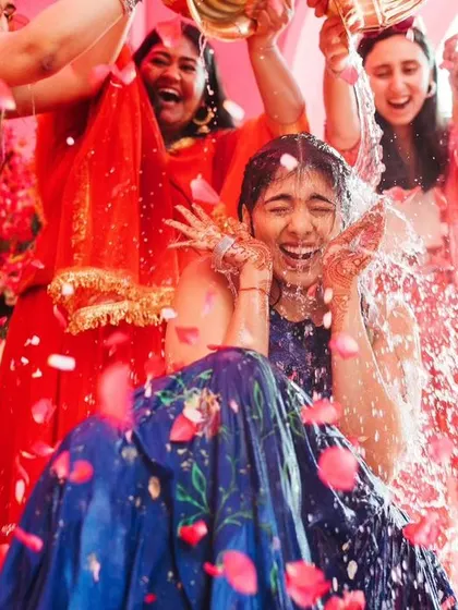 The bride getting drenched in a shower of water and petals, a moment of pure fun and celebration at her Haldi.
