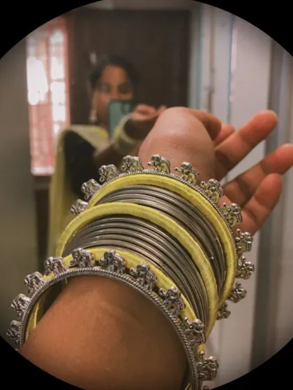 A close-up of the custom yellow and silver bangle set, combining yellow silk thread bangles with oxidised silver elephant-motif kadas.