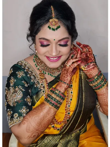 A candid moment of Akshatha during her Varapooja, adjusting her earrings and showing off her intricate henna and festive makeup.