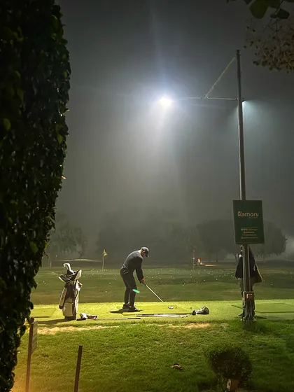 A lone golfer practices chipping under the spotlight on a misty evening, showing the dedication of our community.