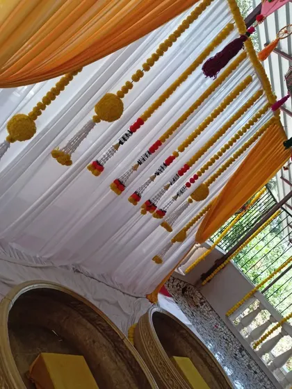 An upward view of the Haldi decor, showing the details of the yellow drapes, marigold tassels, and the colorful umbrella ceiling.