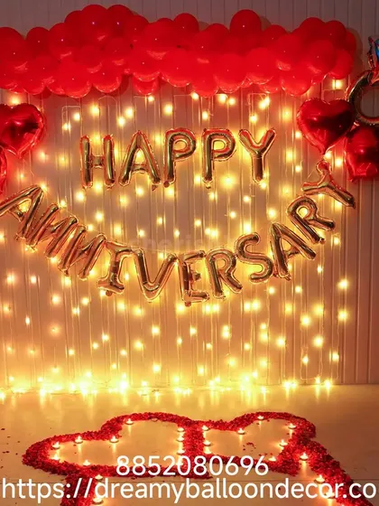 A romantic anniversary backdrop featuring a wall of fairy lights. The 'Happy Anniversary' foil balloons and red heart accents create a warm and loving glow.
