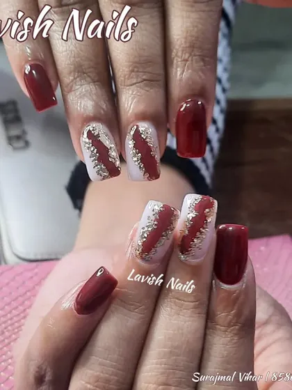 A bold design with deep red polish and accent nails featuring a dramatic slash of gold foil on a white base.