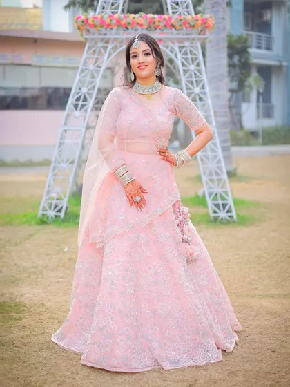 A full-length portrait of a woman in a lovely pink lehenga for a pre-wedding event.