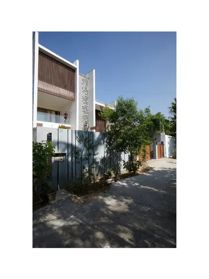 The entrance to the Vikas Residence is set back from the street, creating a quiet, shaded approach. The design plays with solid and void, using a simple grey fence and lush planting to create a gentle transition into the home.