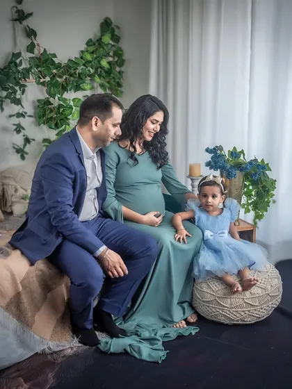 A family portrait from a maternity session, featuring the parents-to-be and their young daughter. The cozy, stylish studio setting provides a warm and inviting backdrop for this family memory.