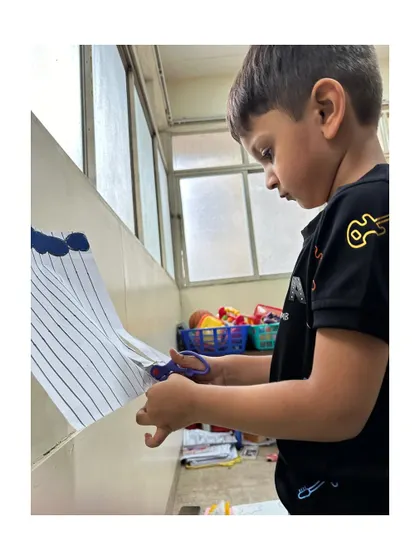 We provide careful guidance during scissor practice. This activity is crucial for developing the precision and control needed for pre-writing skills and other detailed tasks.