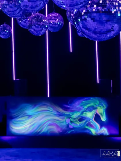 A custom-painted bar front featuring a celestial horse, illuminated by UV light. This artistic detail, set under a canopy of disco balls, was a major highlight of our vibrant after-party.